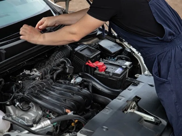 FAM szerelő az akkumulátort szereli a jármű motorterében